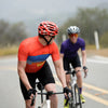 Male road cyclist in orange revel jersey being chased by female cyclist in purple Motion jersey in Malibu California