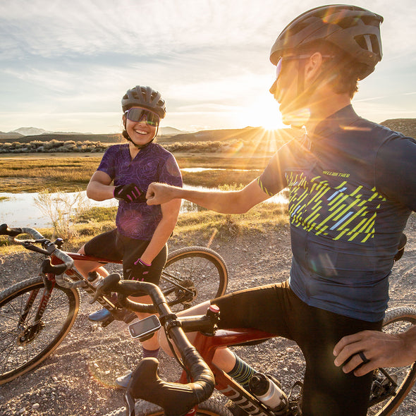 Male and female gravel cyclists fist bump after gravel ride as the sun is setting 